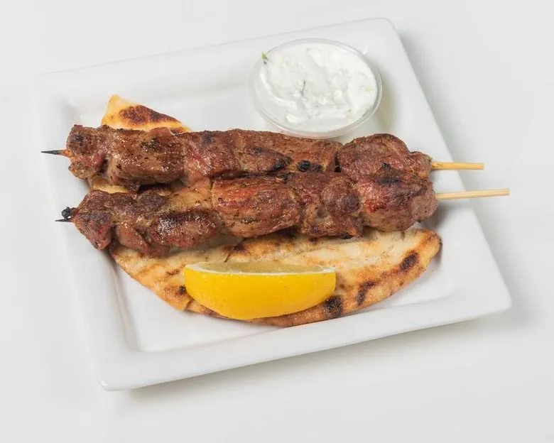 Two pork souvlaki skewers on pita with lemon and tzatziki